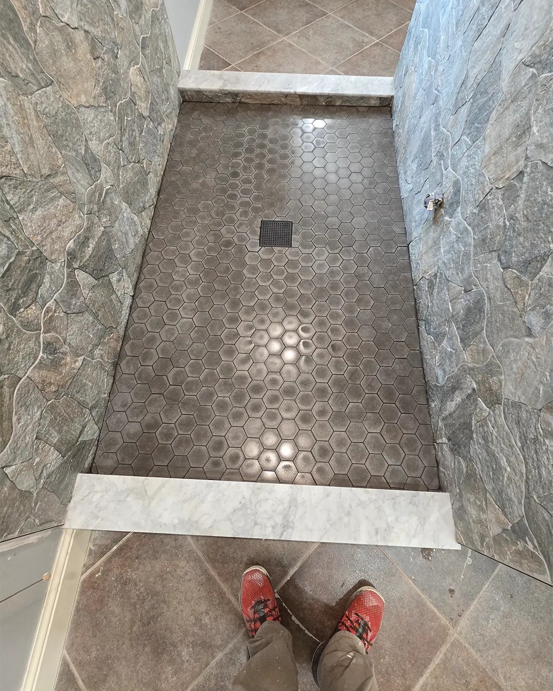 Hexagon tile shower pan with marble curb and stacked stone walls